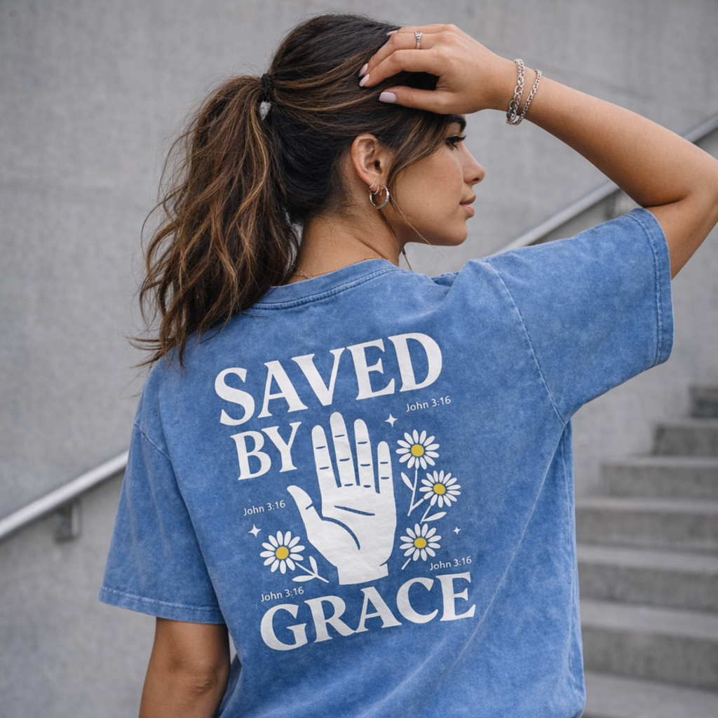 Woman wearing a blue t-shirt with 'Saved by Grace' text and daisy design.